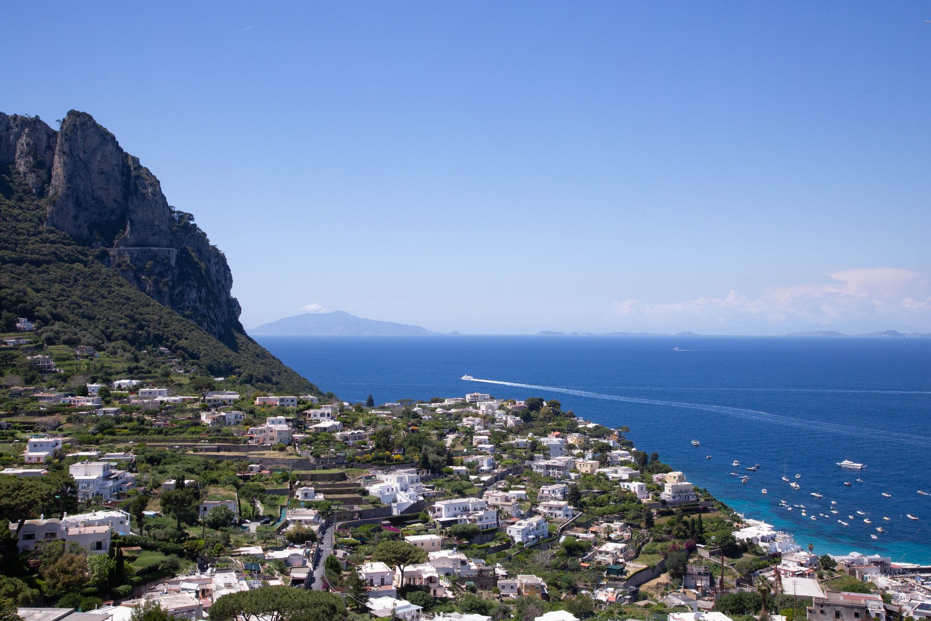 Coastal hillside town on Capri Island with white houses, blue ocean, and rocky cliffs under a clear sky