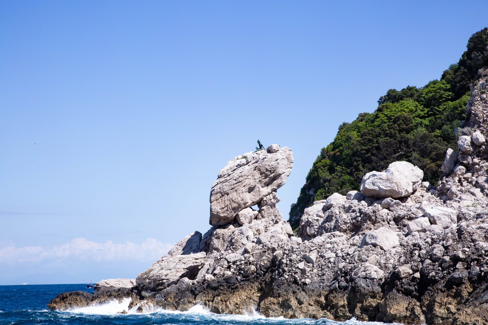 Rocky seaside cliffs with waves and clear blue sky, with small birds perched on the tallest rock