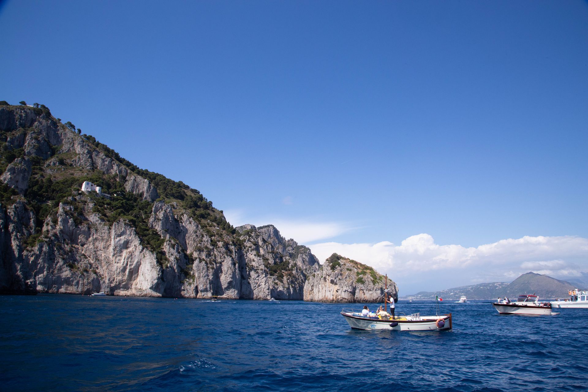 Cliffs along a blue sea with boats under a clear sky