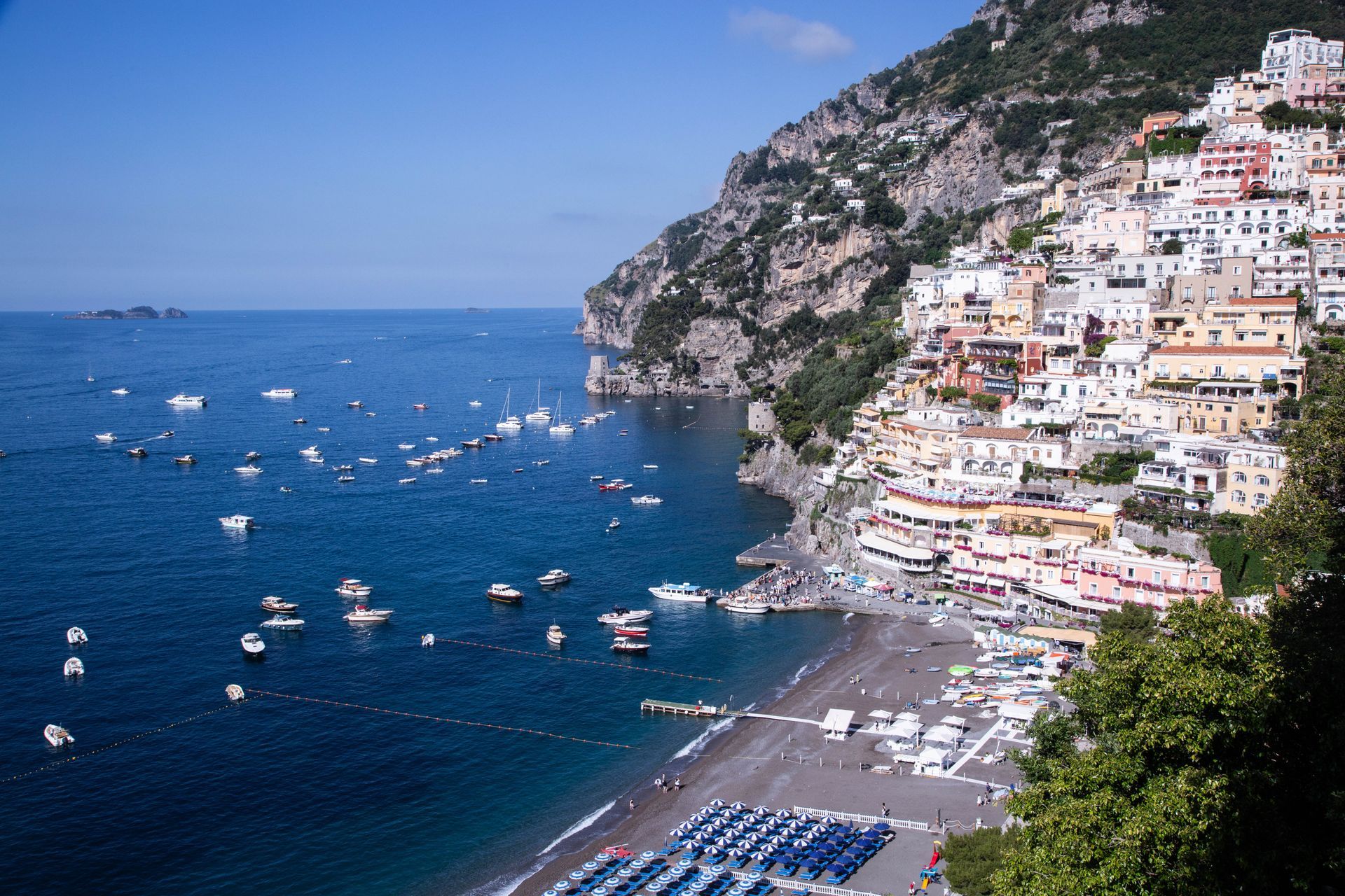 Coastal cliff town with white buildings overlooking a blue bay full of boats