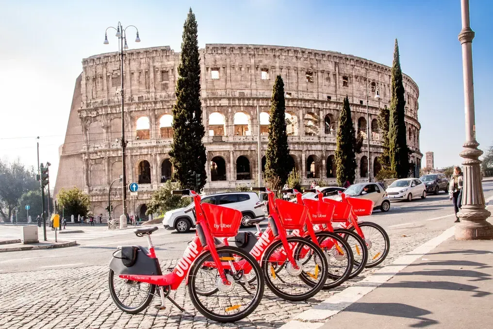 Red rental bikes parked in front of the Colosseum in Rome, Italy.