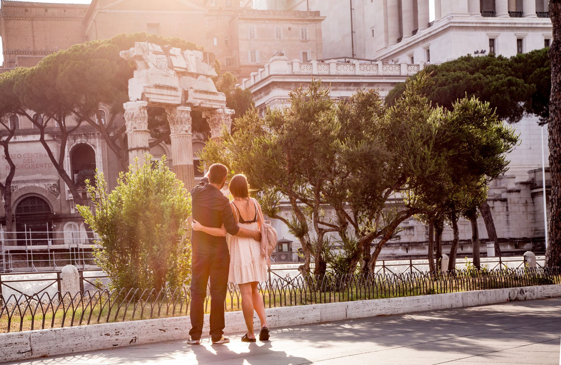 Couple embraces, looking at ruins in Rome at sunset.
