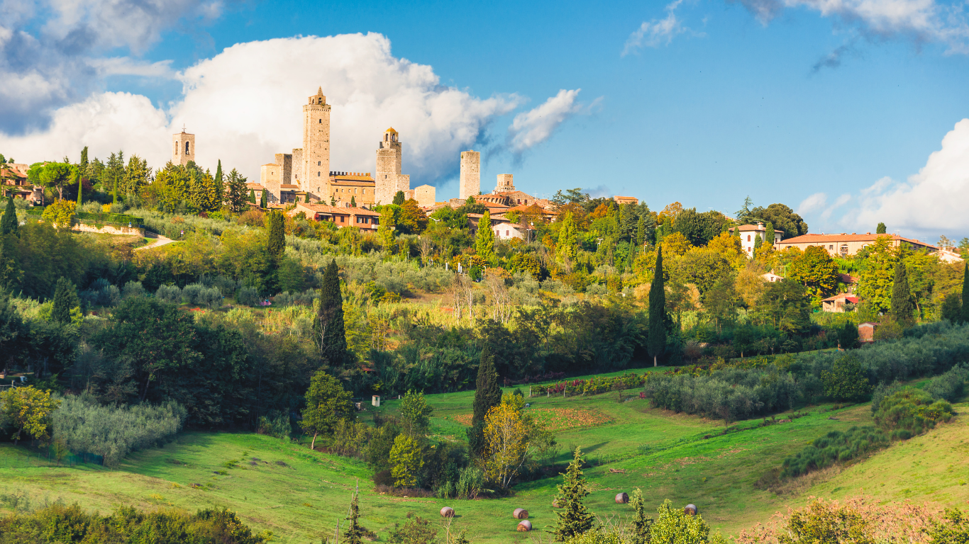 Sunlit hilltop cathedral and towers above lush green gardens under a blue sky