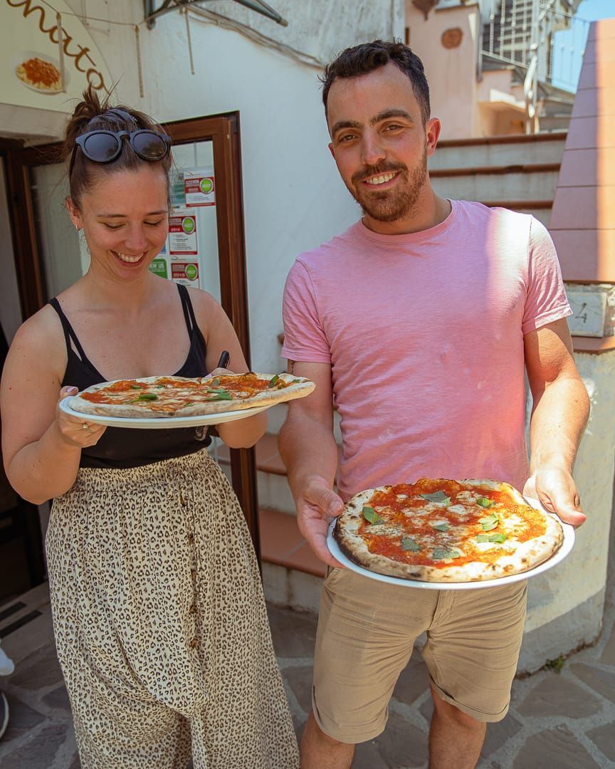 Couple holding pizza they made in the pizzeria.