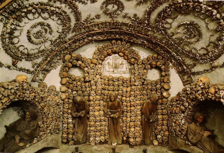 Chapel decorated with skulls and bones; figures in brown robes stand before an altar.