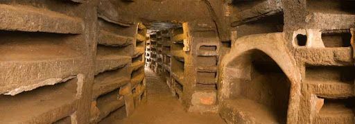 Tunnel with many burial niches carved into the walls, likely catacombs.