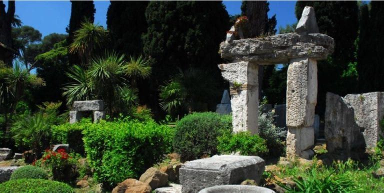 Stone ruins and lush greenery in a garden on a sunny day.