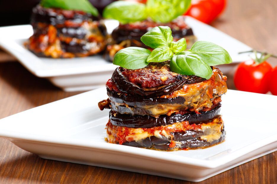 Eggplant stacks with tomato sauce, cheese, and basil on white plates.