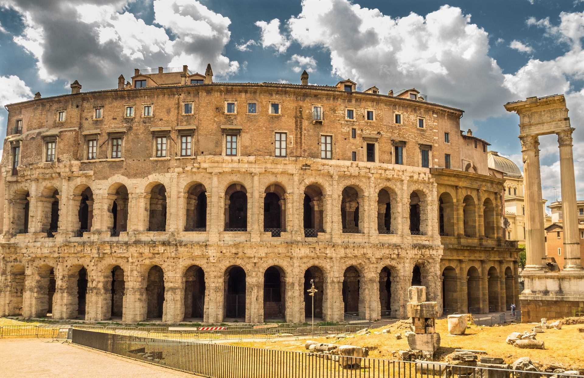 Ancient Roman theater ruins in Rome, Italy, with arched structures and partial columns under a cloudy sky.