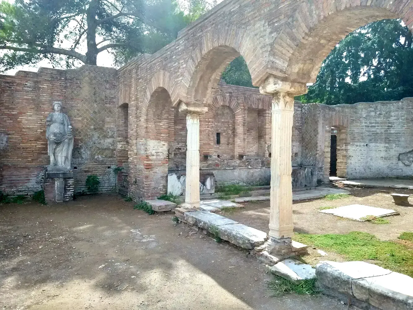 Ruins of ancient Roman bathhouse with arches and statue.