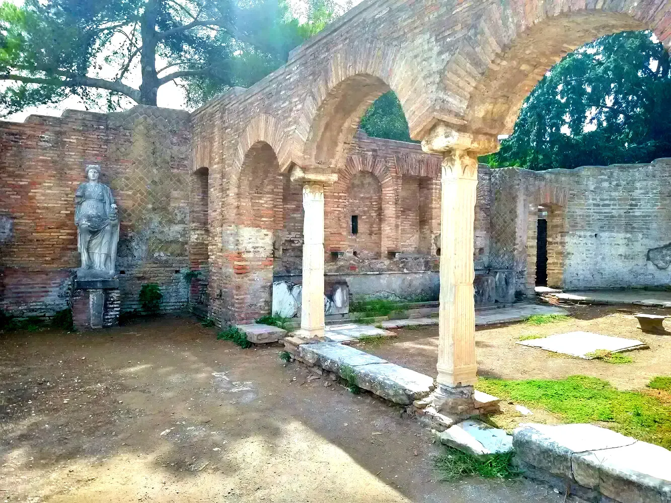Ancient Roman ruins: Arches, columns, brick walls, statue, and dirt ground.