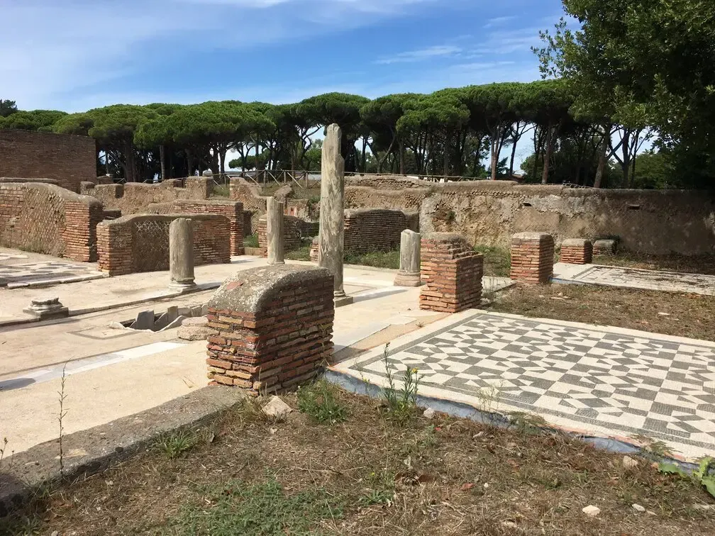 Ruins of Ostia Antica, Italy, showcasing brick and stone structures, columns, and mosaic flooring under a blue sky.