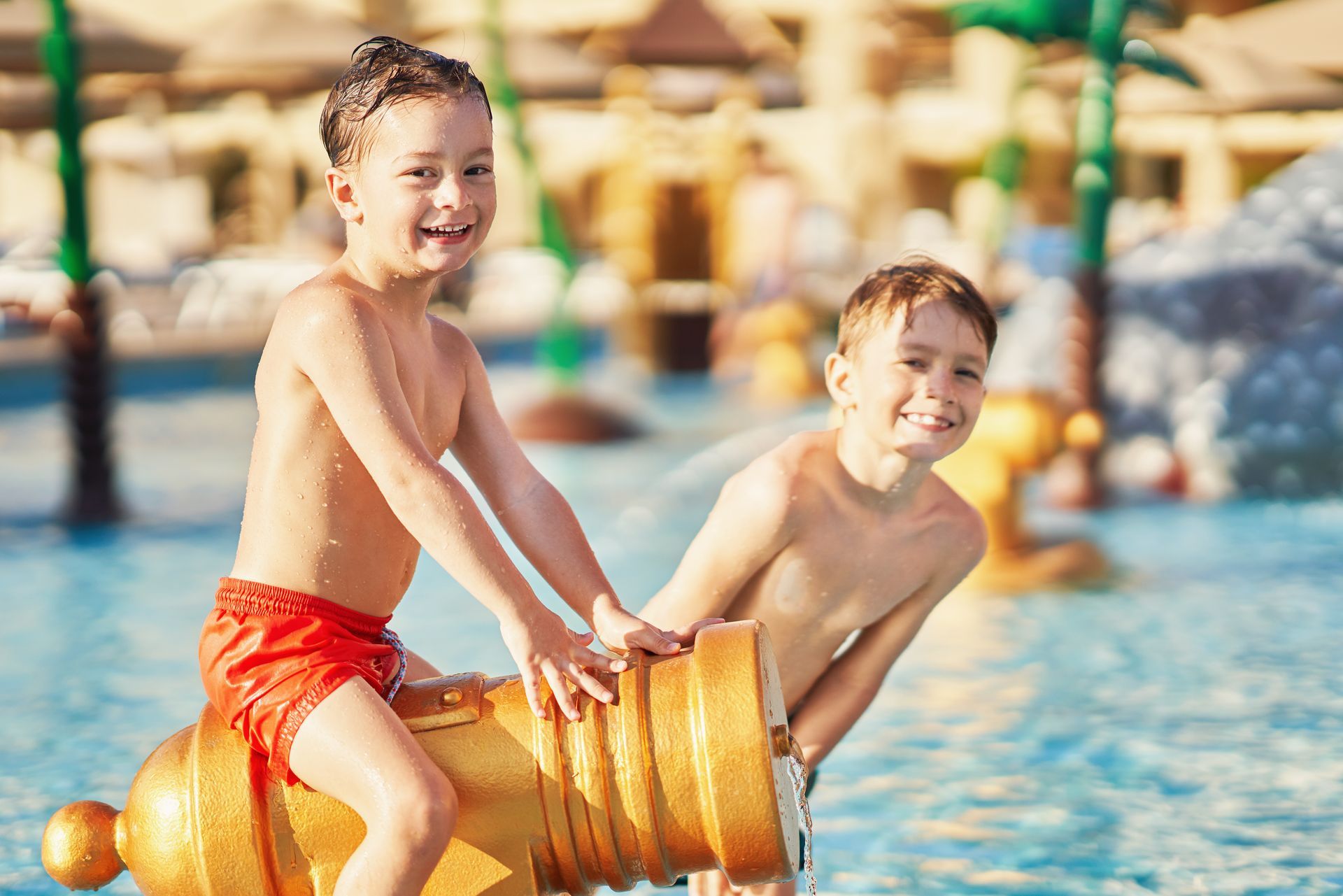 Two boys smiling, playing with a water cannon in a pool at a water park.