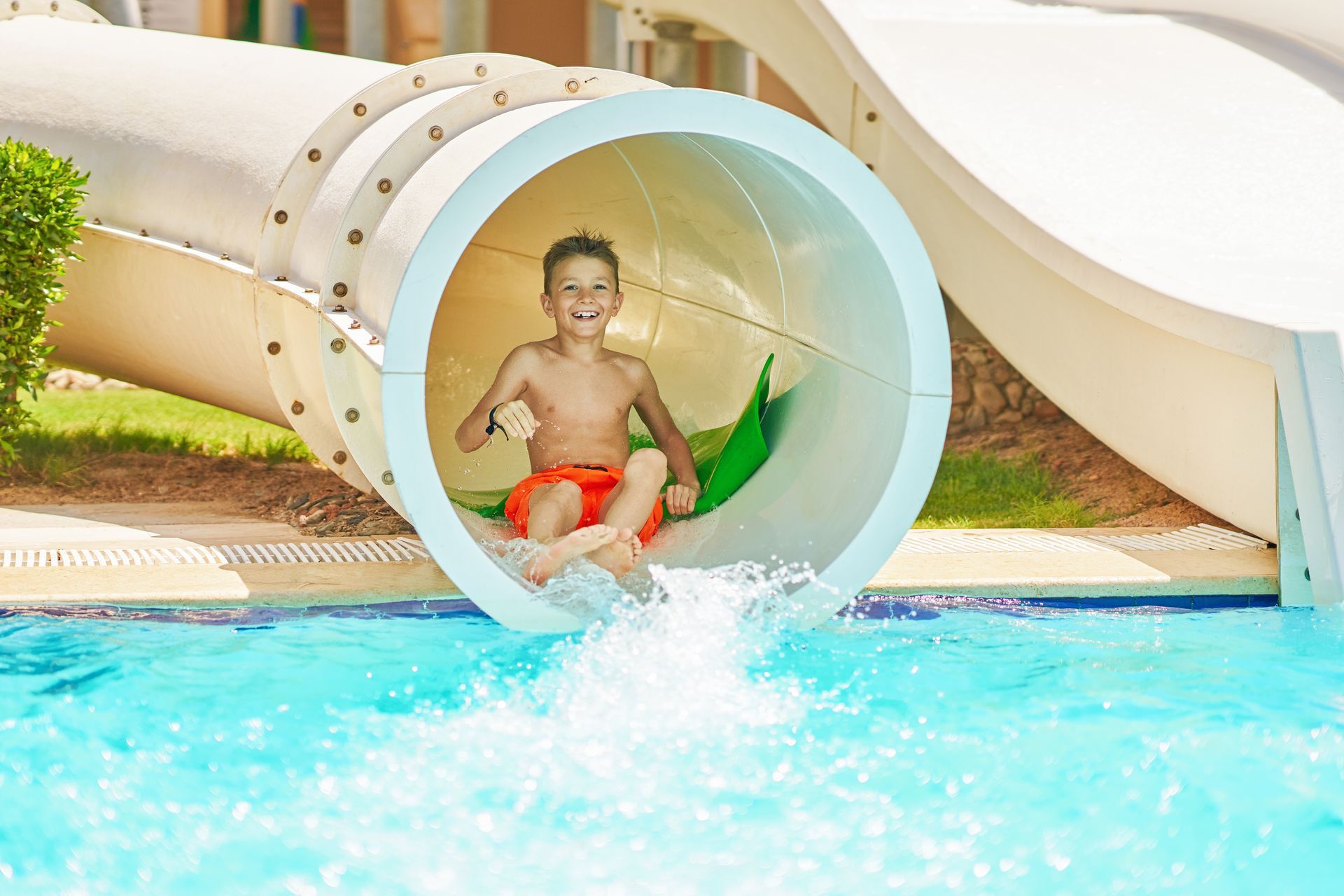 Boy sliding down a water slide into a pool, with splash.