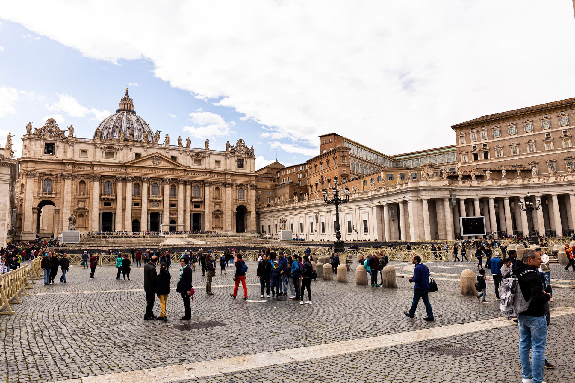 St. Peter's Basilica, Rome, with tourists in the square under a cloudy sky.