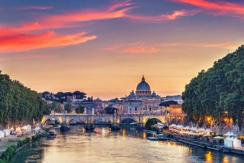 Sunset over the Tiber River in Rome, St. Peter's Basilica in the distance, with a colorful sky.