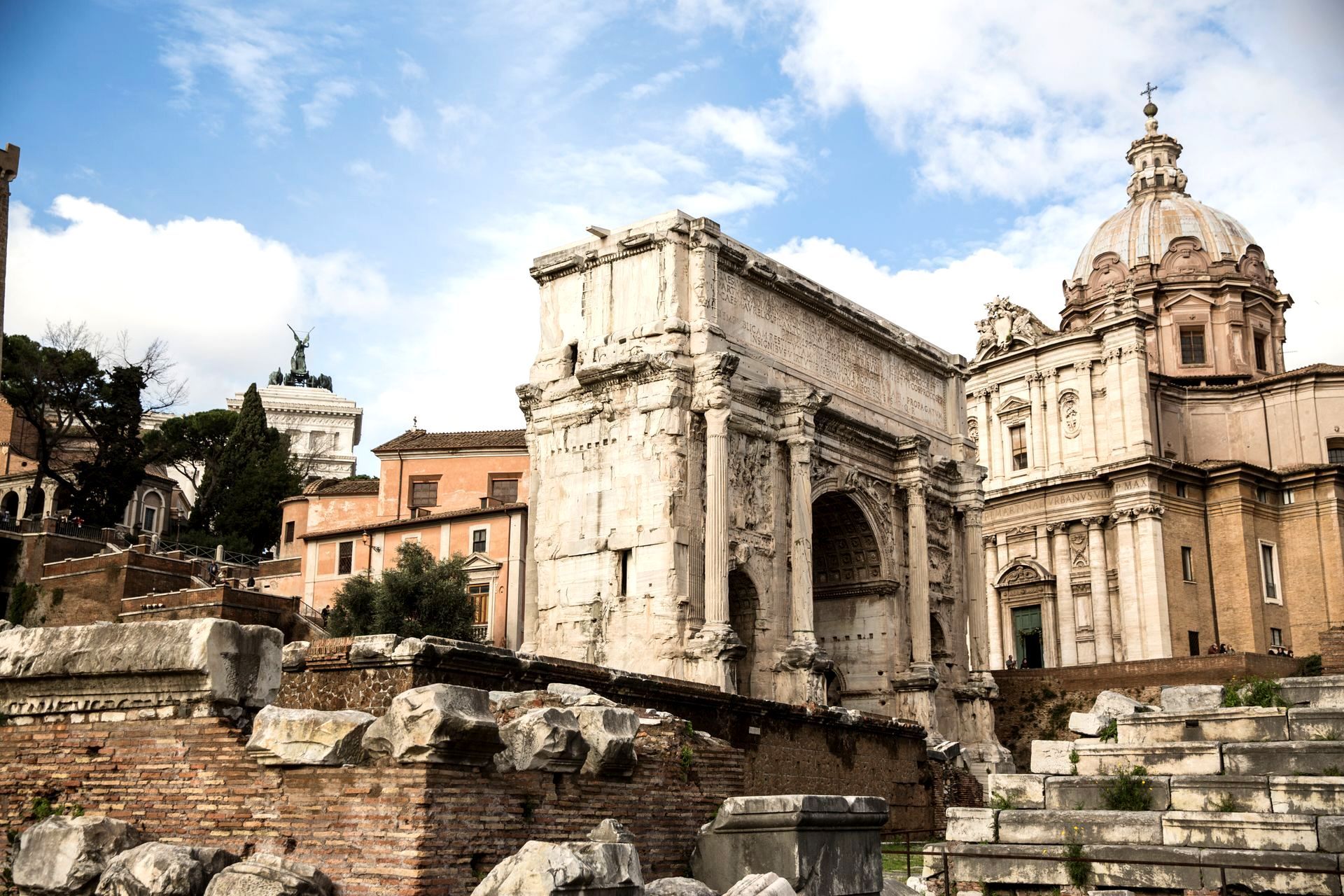Ancient Roman ruins including arch and domed building under a blue sky.