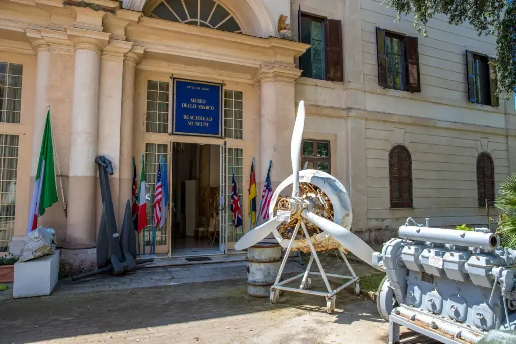 A museum entrance with an airplane propeller and engine on display, with flags outside.
