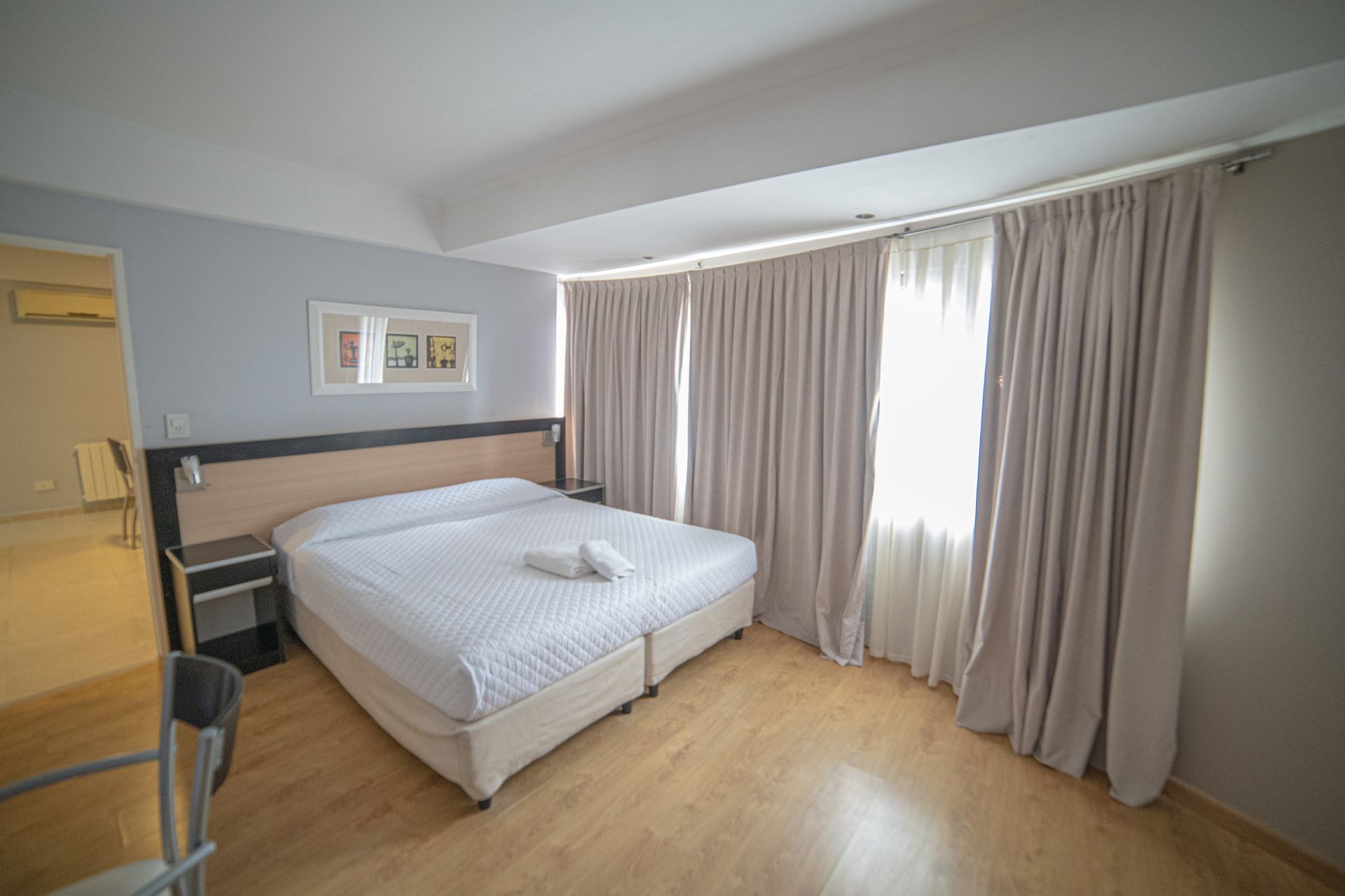 Hotel bedroom with a bed, windows, and light-colored curtains.