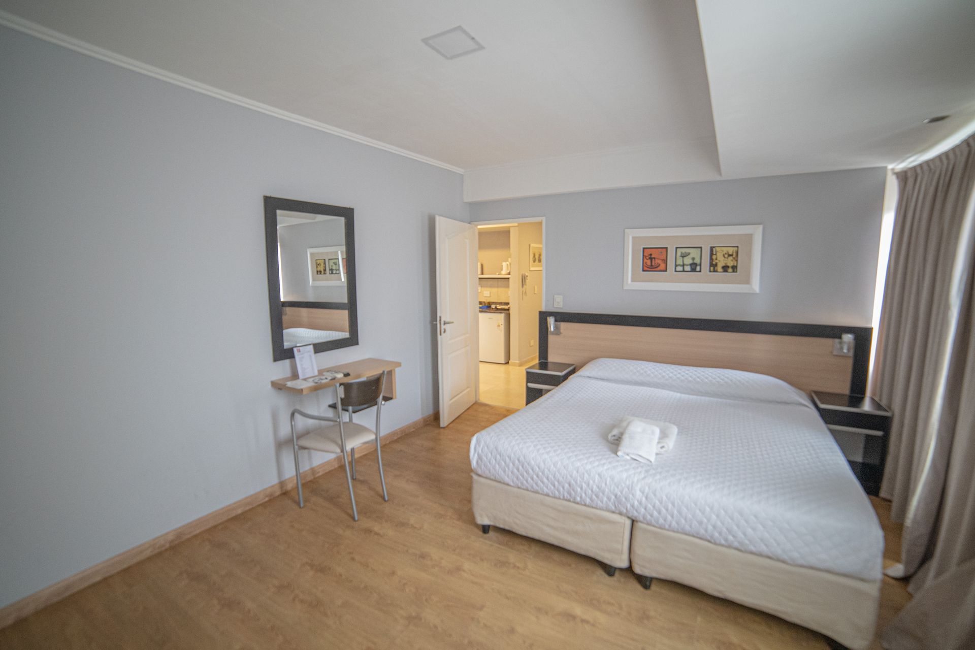 Hotel room with bed, desk, mirror, and open door to another room.
