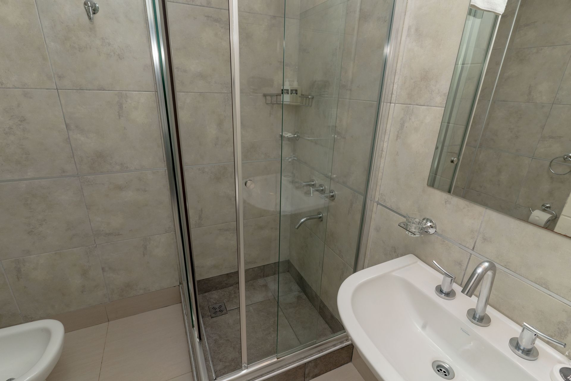 Bathroom with shower stall, sink, and toilet. Light-colored tile walls, glass shower door, and chrome fixtures.