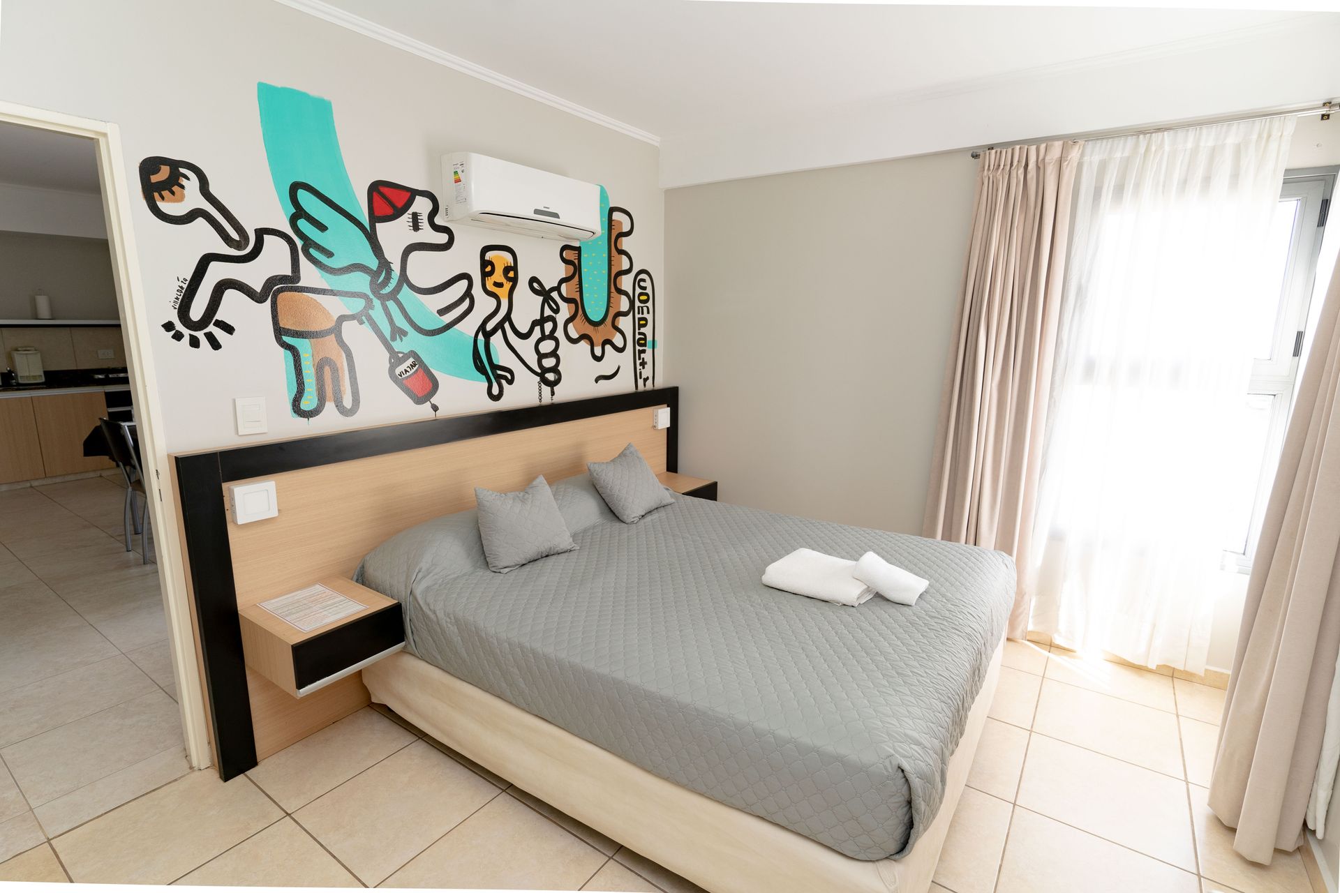 Bedroom with graffiti wall art, bed with gray bedding and pillows, and a window with curtains.