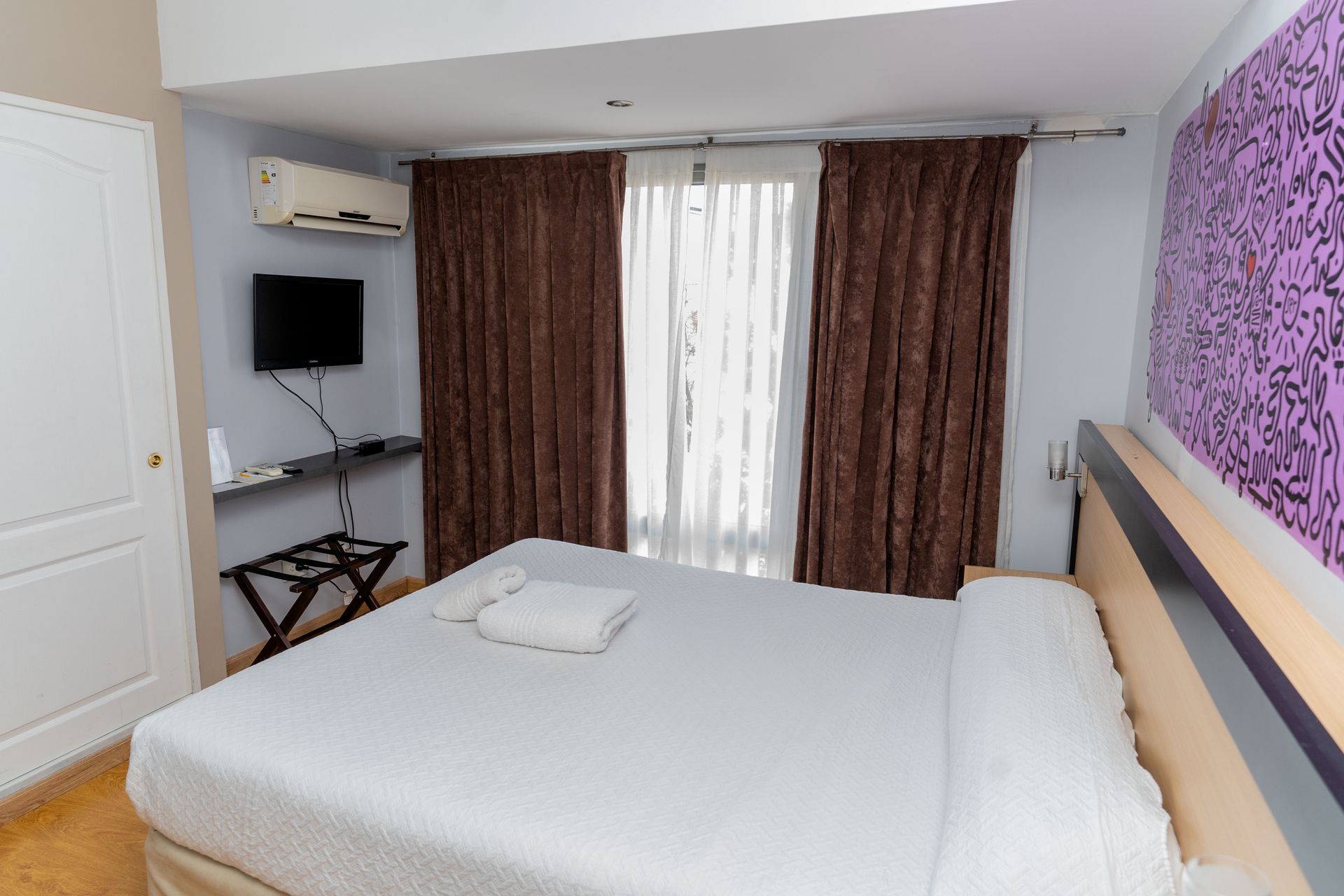 Hotel room with a bed, TV, and brown curtains.