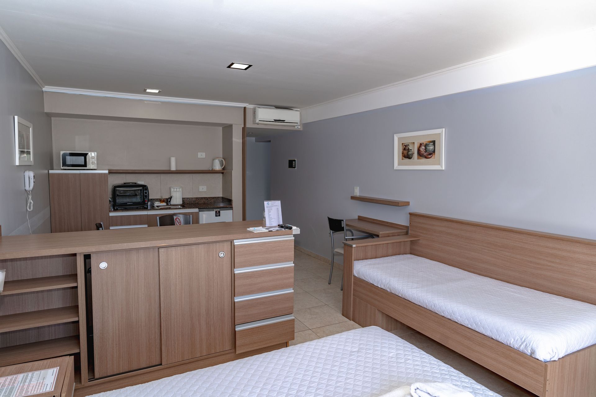 Studio apartment interior: wooden furniture, kitchen area, two beds, gray walls.