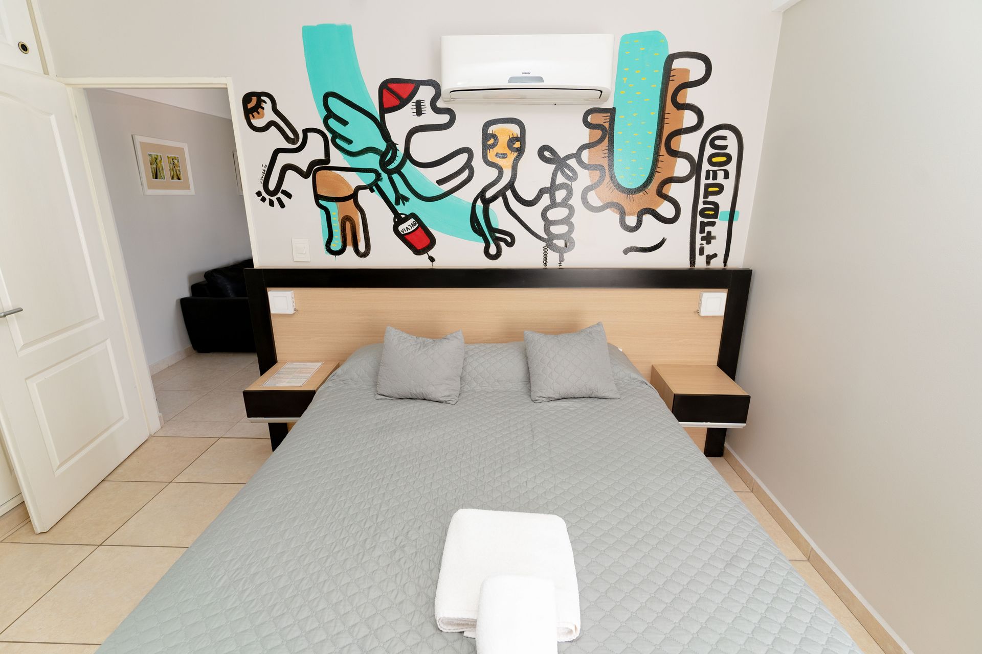 Bedroom with a bed, nightstands, and graffiti art on the wall. A/C unit is above bed.