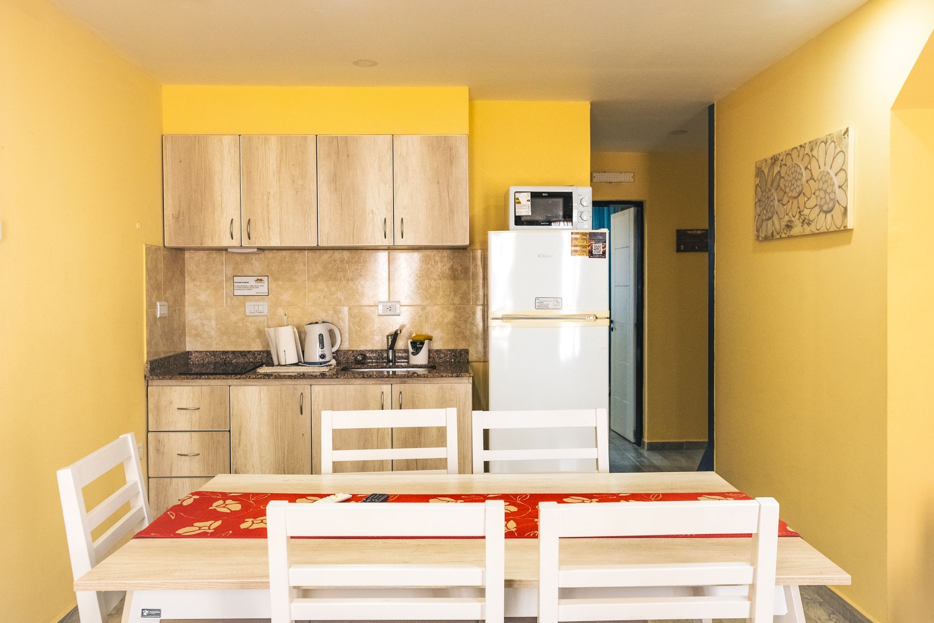 Kitchen with light wood cabinets, white table and chairs, yellow walls, and a refrigerator.