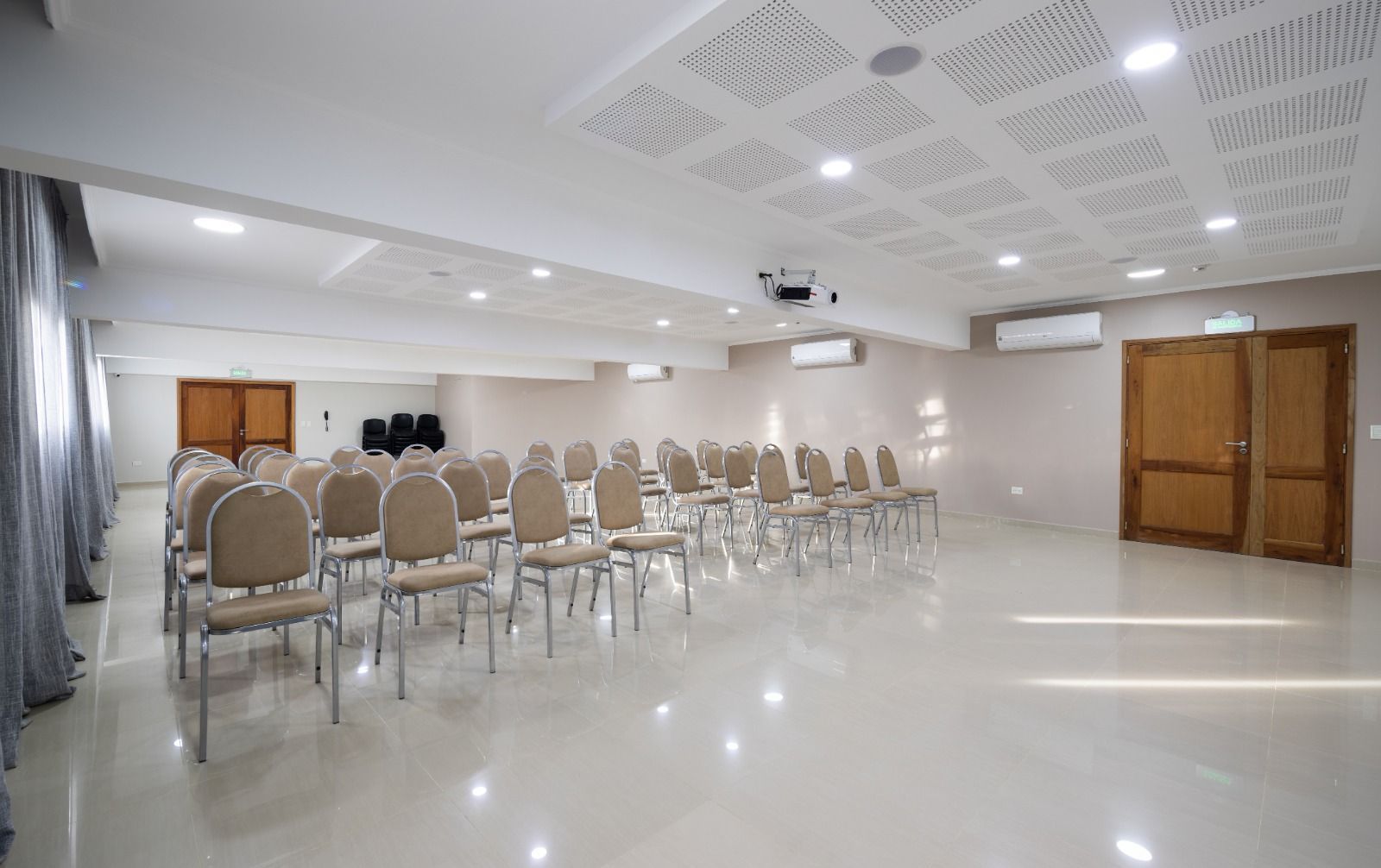 Empty conference room with rows of chairs, projector, and wooden doors.