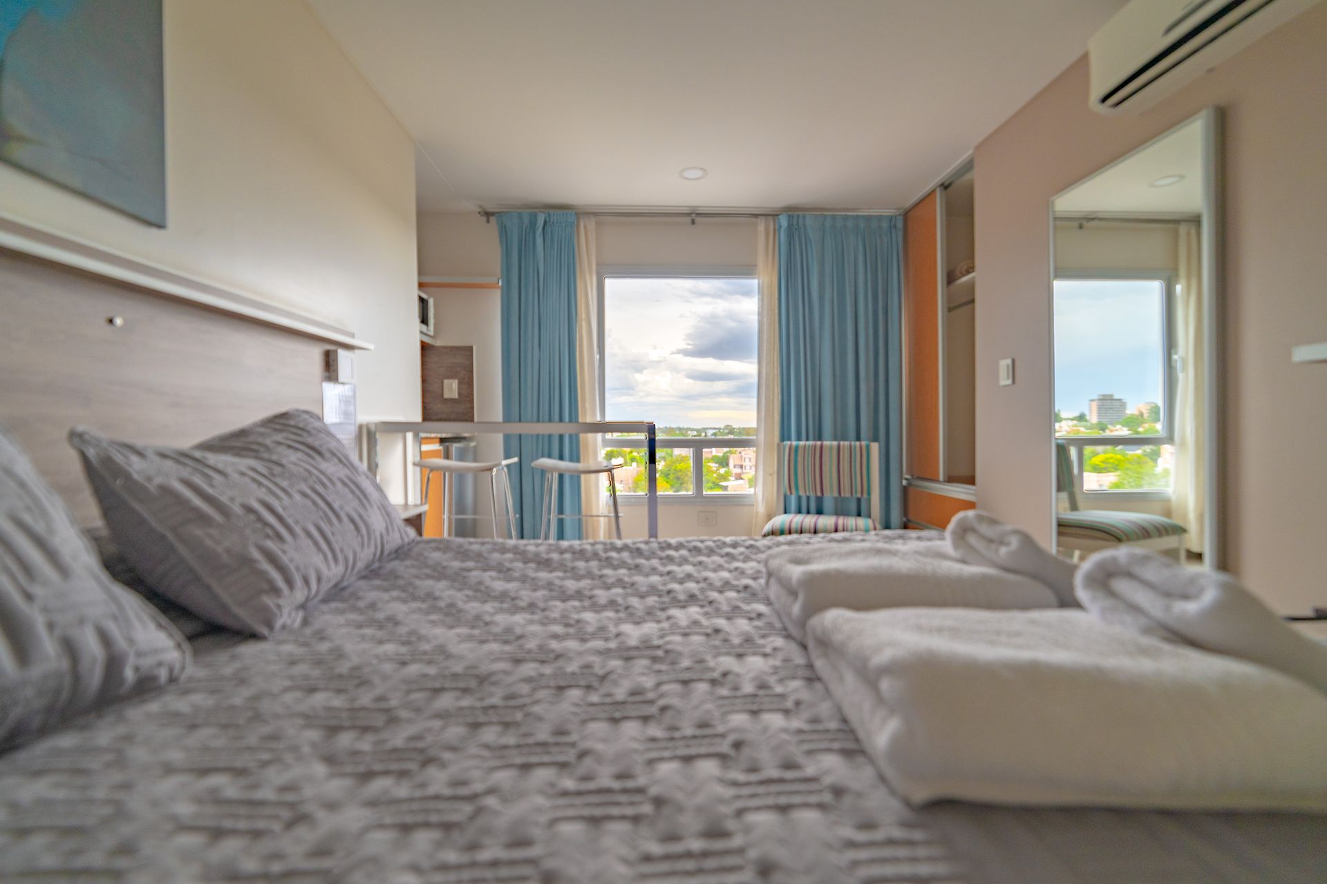 Bedroom with bed, blue curtains, and a window overlooking a cityscape.