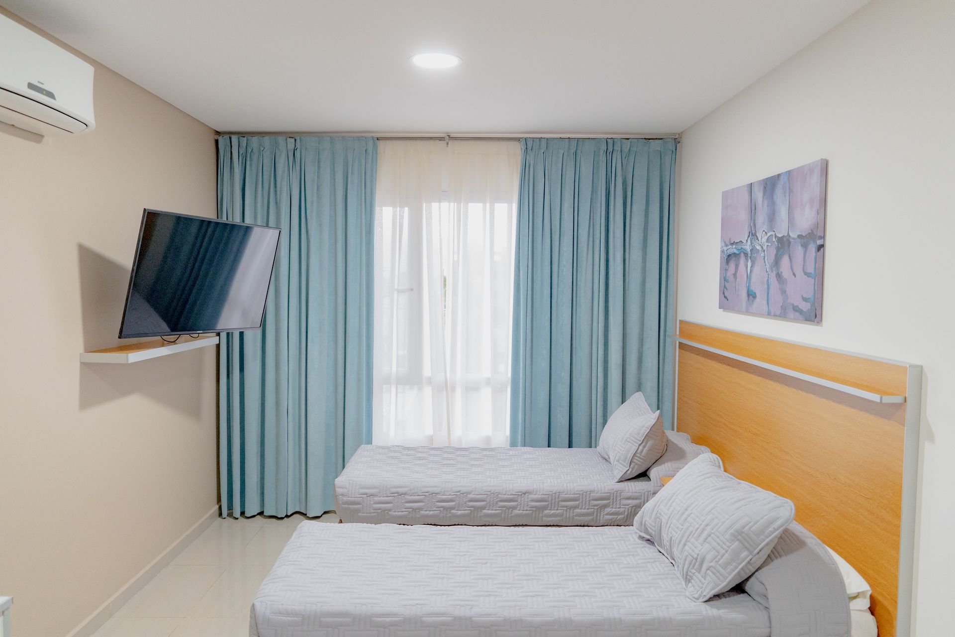 Bedroom with two twin beds, light blue curtains, TV, and artwork.