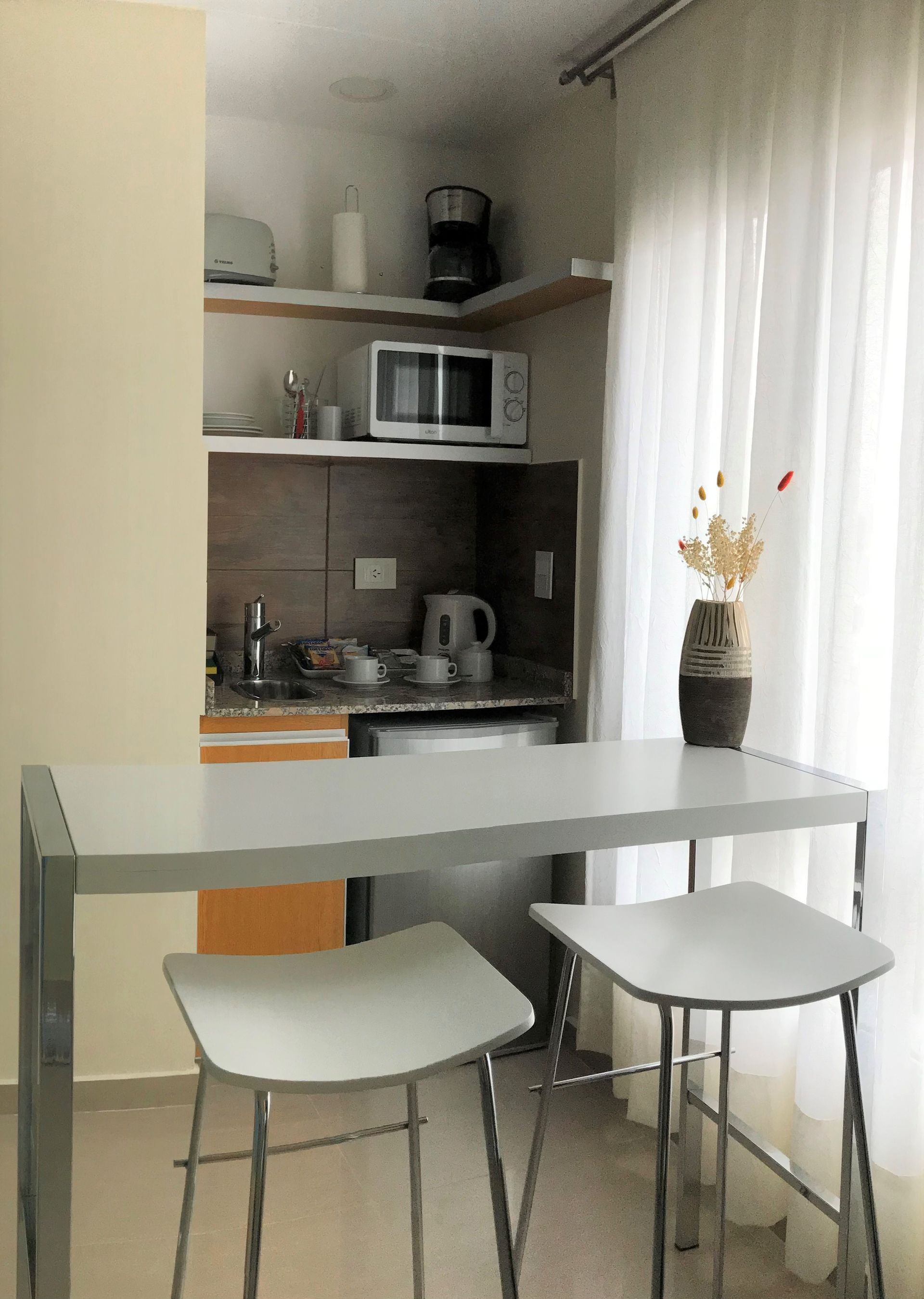Small kitchen with countertop and two stools. Appliances include a microwave, coffee maker, and toaster.