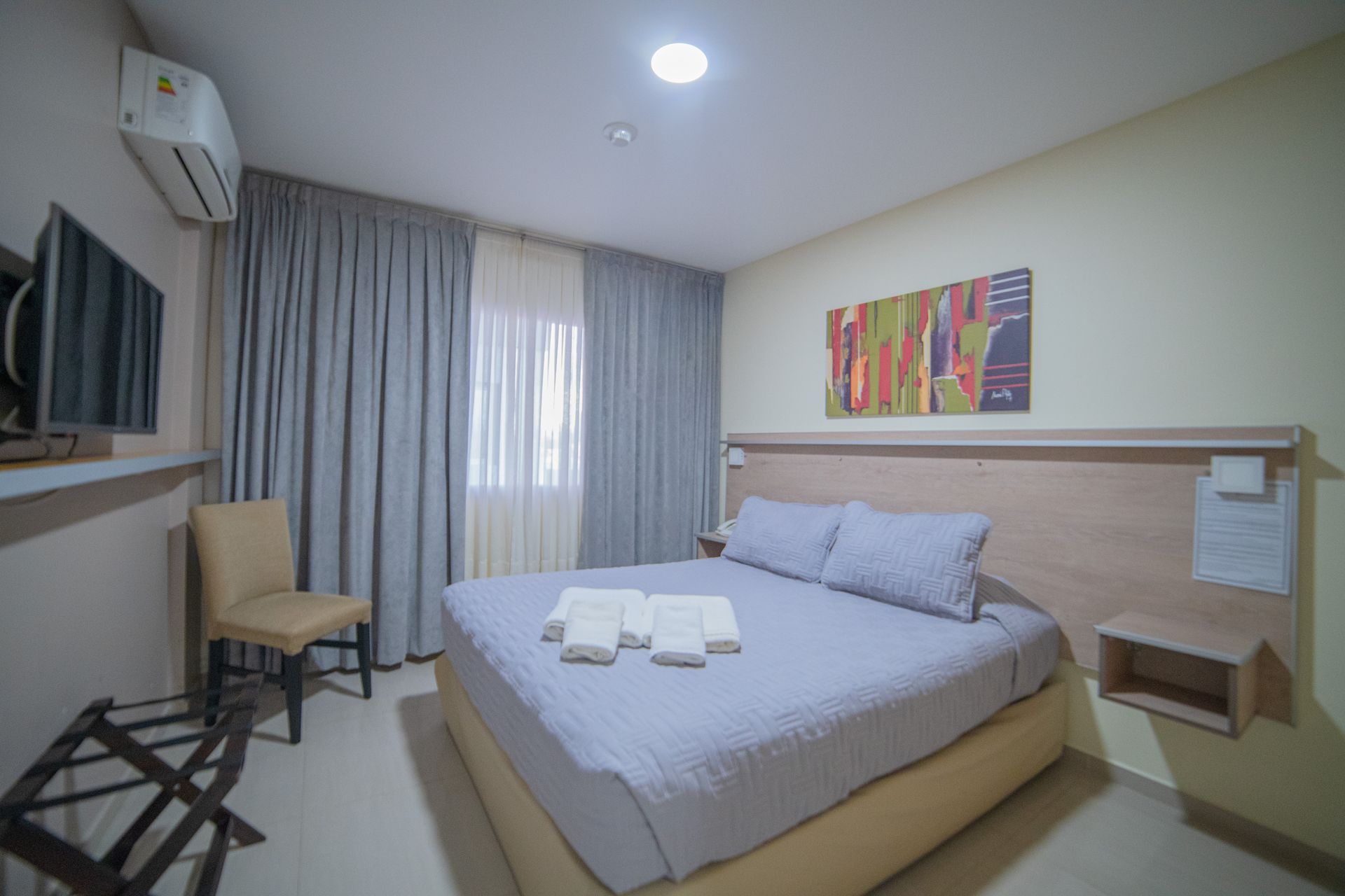Hotel bedroom with a bed, TV, chair, and luggage rack.