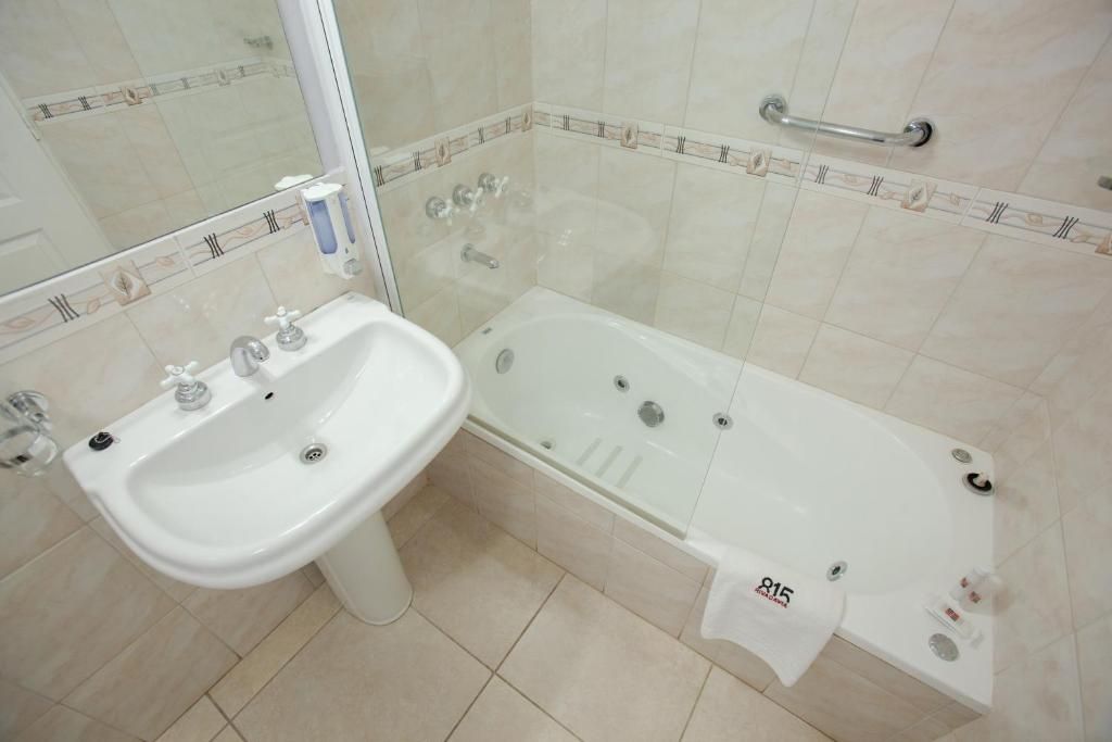 Bathroom with white pedestal sink, jacuzzi tub, and tiled walls.