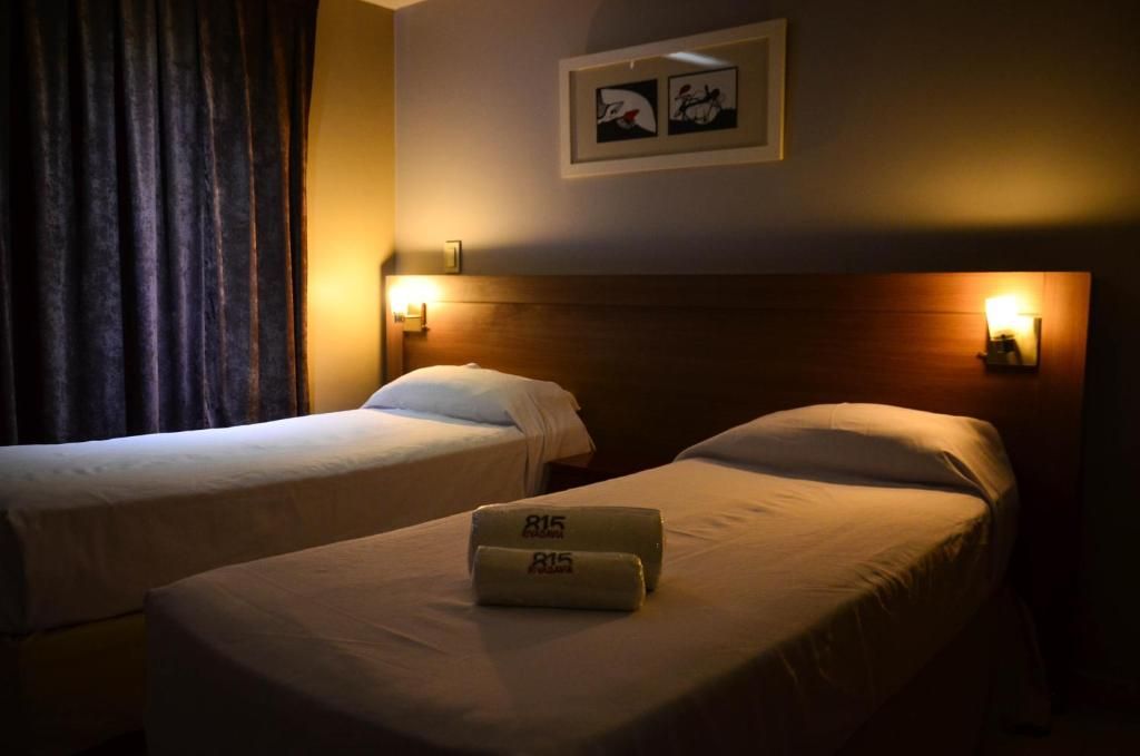 Two twin beds in a dimly lit hotel room with a framed picture and bedside lamps.