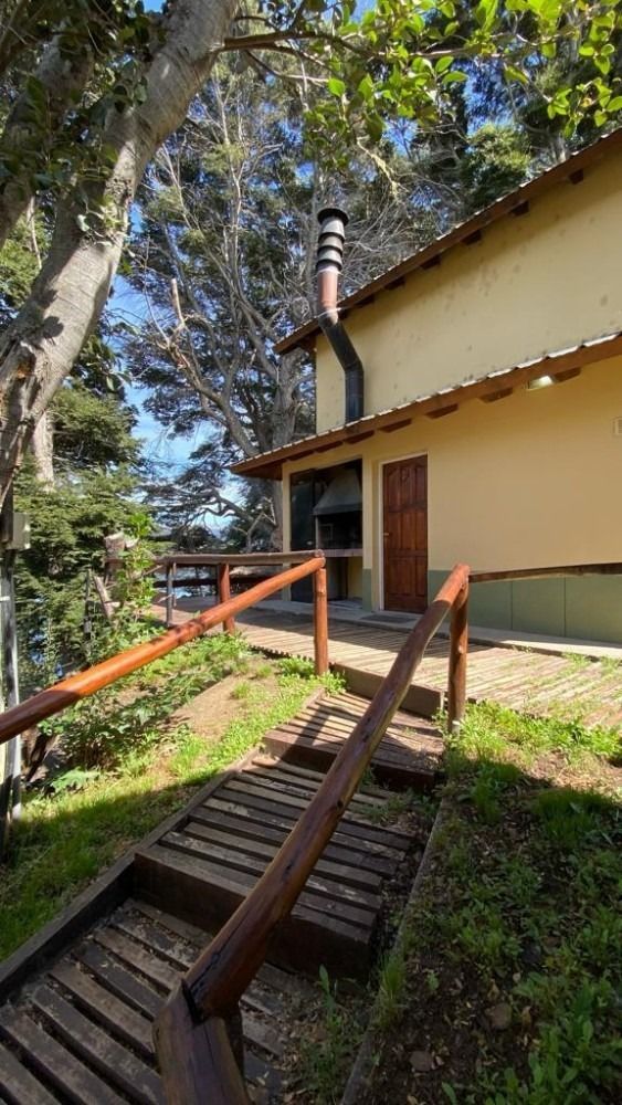 Wooden steps lead up to a light-yellow building with a chimney and wooden door, set among trees.