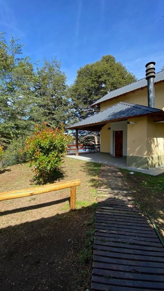 Wooden walkway leads to a beige house with a covered porch under a bright blue sky.