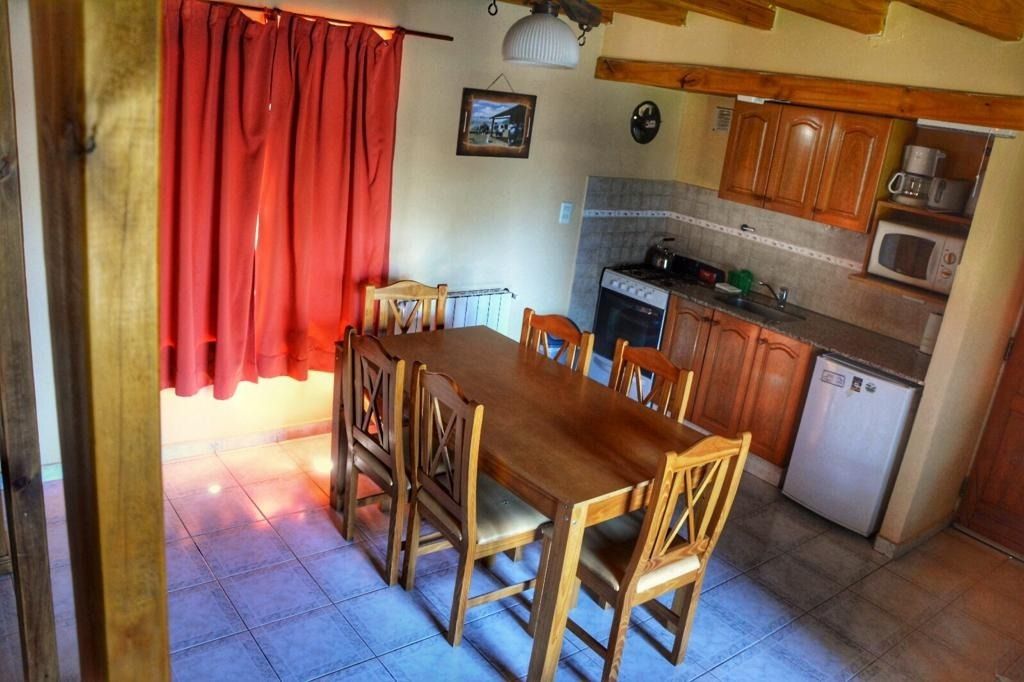 Kitchen and dining area with wooden table, chairs, cabinets, red curtains, and appliances.