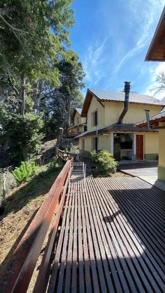 Wooden walkway leading to yellow buildings with chimneys, set in a wooded area under a blue sky.