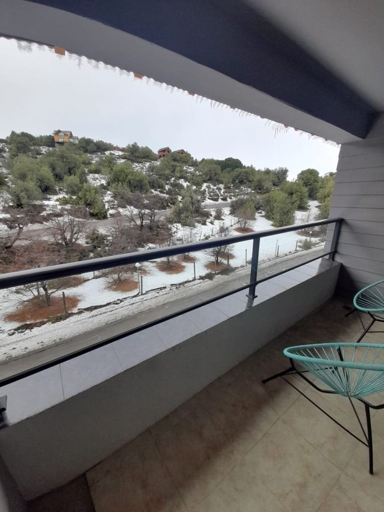 Balcony with snow-covered landscape view. Turquoise chairs on the right. Overcast sky.