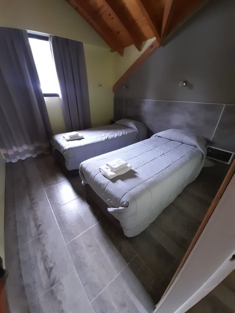 Two twin beds with gray bedding in a room with wood ceiling, window, and gray walls.