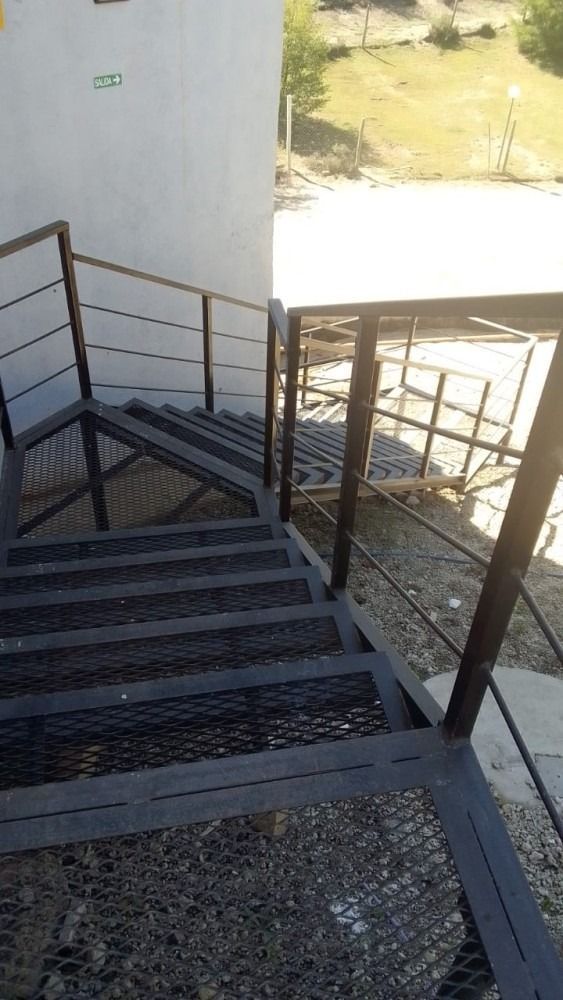 Metal staircase with railings leading to a building. Mesh steps with a light sunny background.