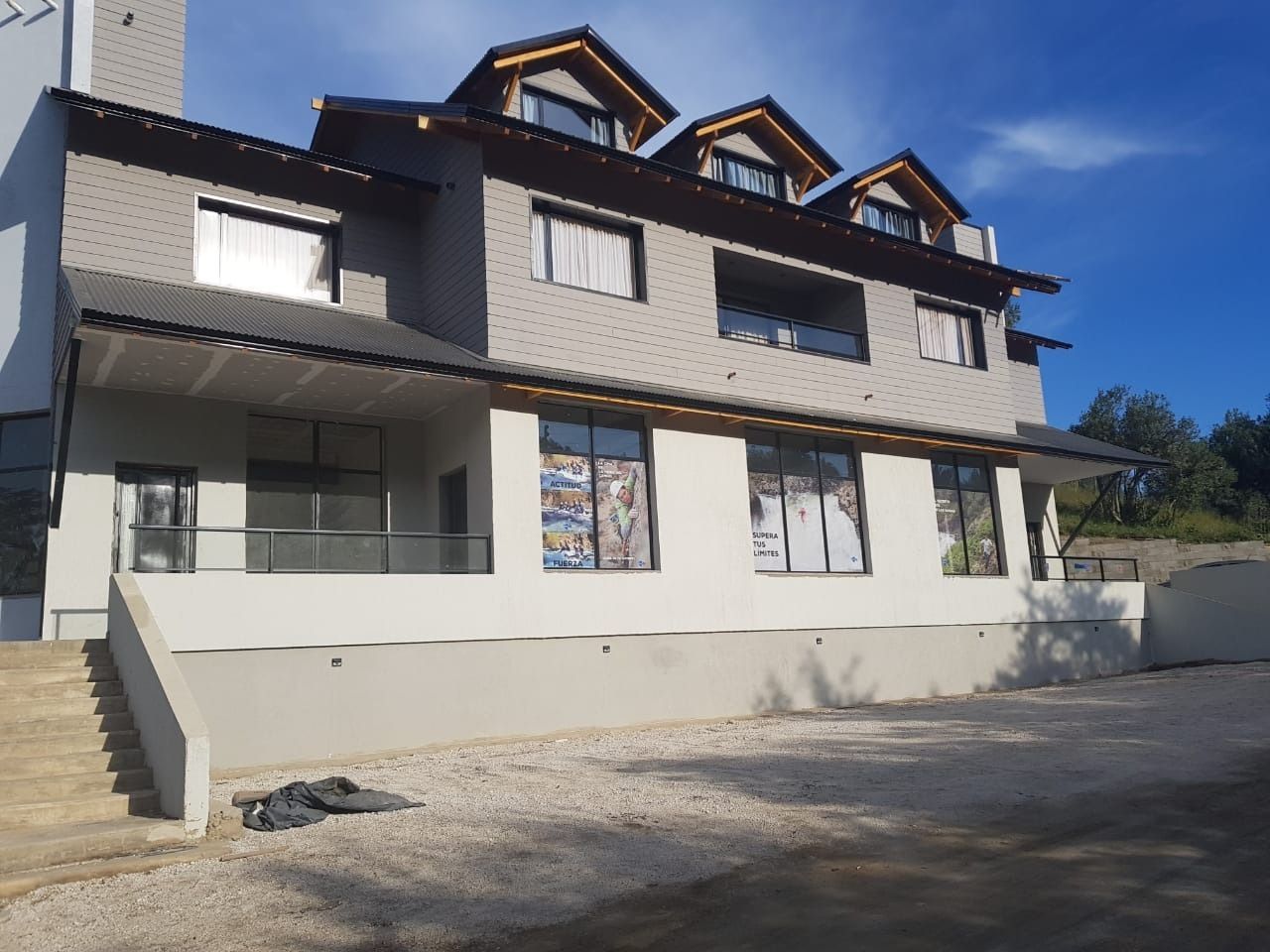 Multi-story gray building with black trim, multiple windows, and a gravel yard.