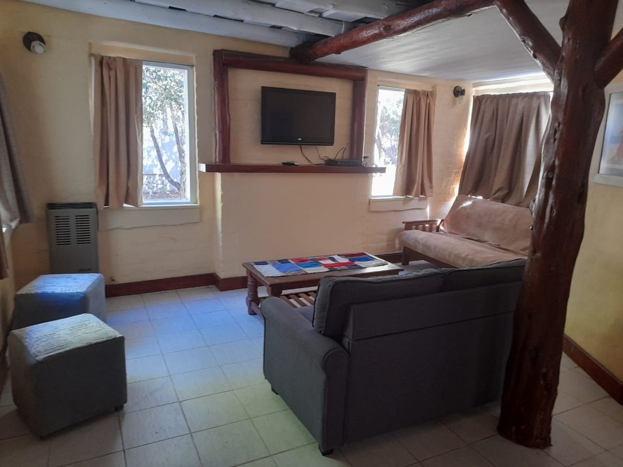 Living room with a TV, couch, chairs, and tree trunk. Window with light-colored curtains. Beige walls.