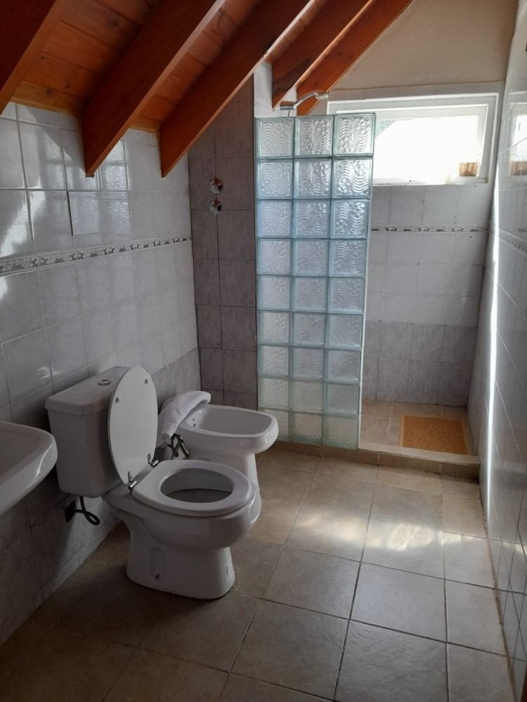 Bathroom with toilet, bidet, and shower stall separated by glass blocks; light tiles, wooden ceiling.