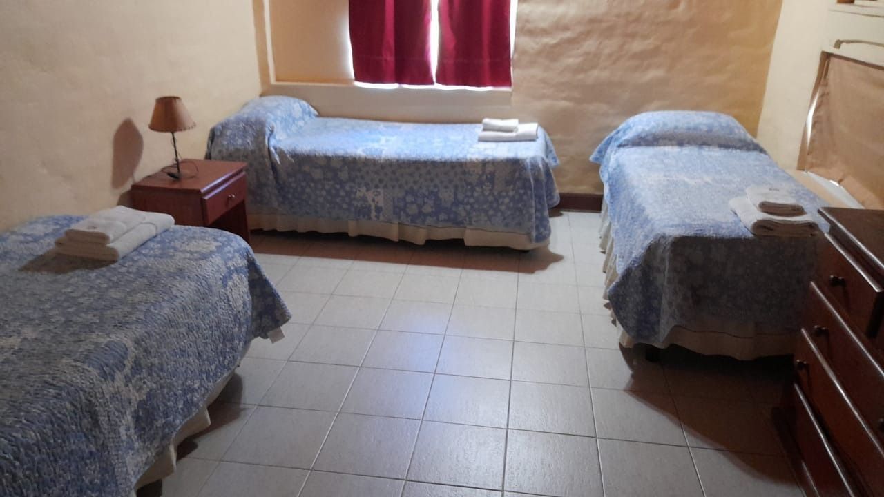 Three beds in a room; each has a blue floral bedspread and a white towel. There is a nightstand and a window.