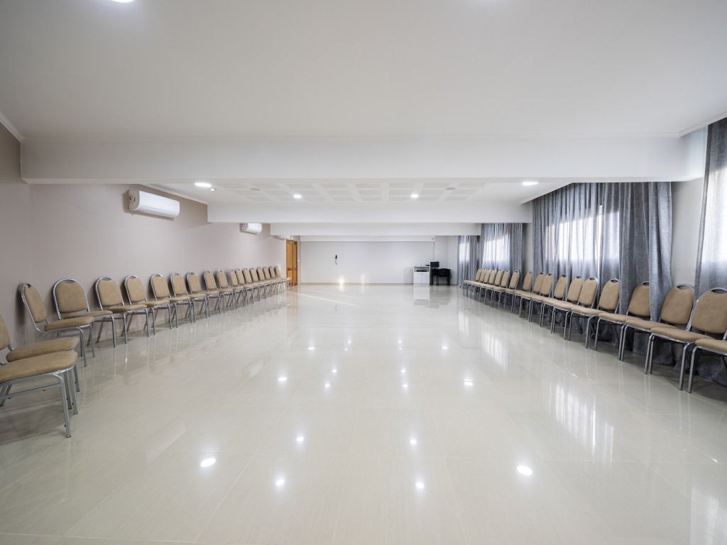 Empty meeting room with rows of chairs, white walls, and shiny floor.