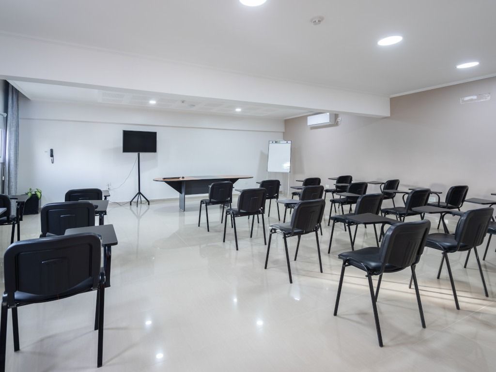 Empty classroom with rows of black chairs, table, and a TV screen.